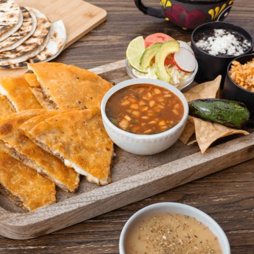 Mexican Mariachi Grill's quesadillas, soup, rice, beans, salad, and tortillas on a wooden tray.