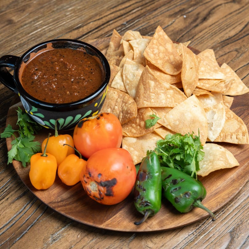 Mexican Mariachi Grill's salsa, tortilla chips, habanero peppers, charred tomatoes, and jalapeños on a wooden board.