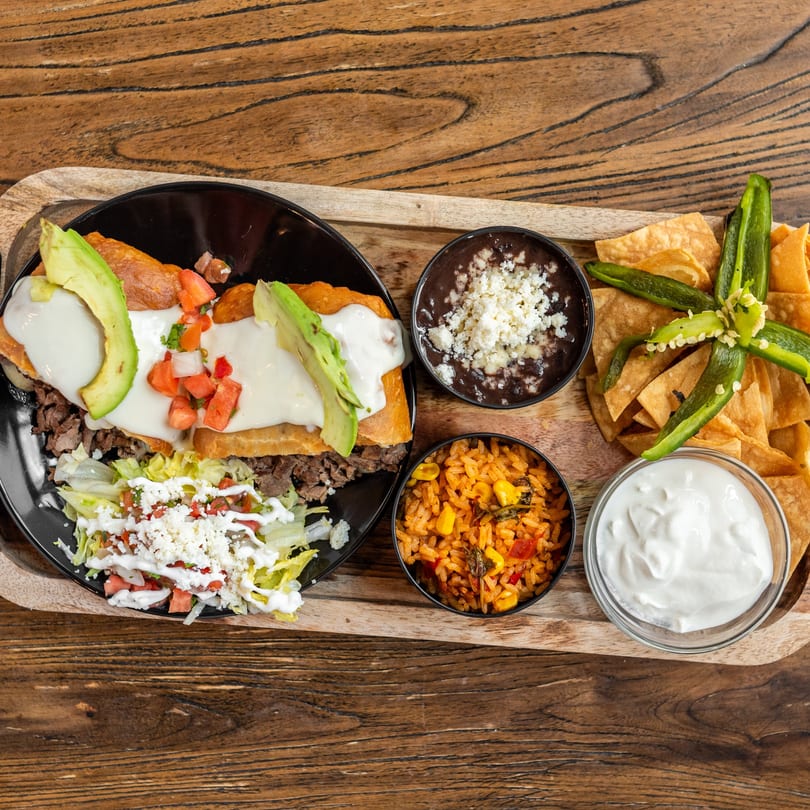 Mexican dish with steak, avocado, and cheese, served with rice, beans, chips, and sour cream.