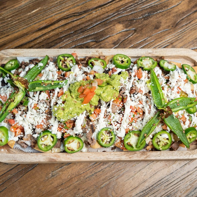Mexican nachos with meat, cheese, guacamole, pico de gallo, and jalapeños on a wooden tray.