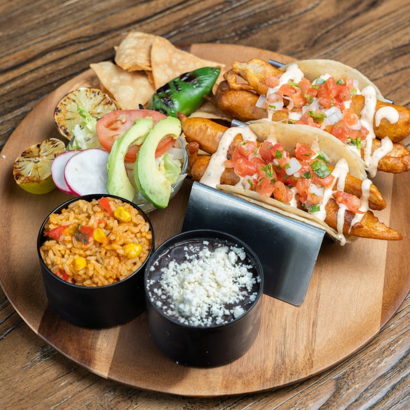 Mexican Mariachi Grill's fish tacos with rice, beans, and salad on a wooden platter.